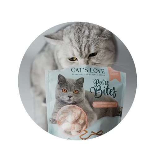 Il gatto si siede dietro una confezione di gamberetti Pure Bites e annusa la confezione.